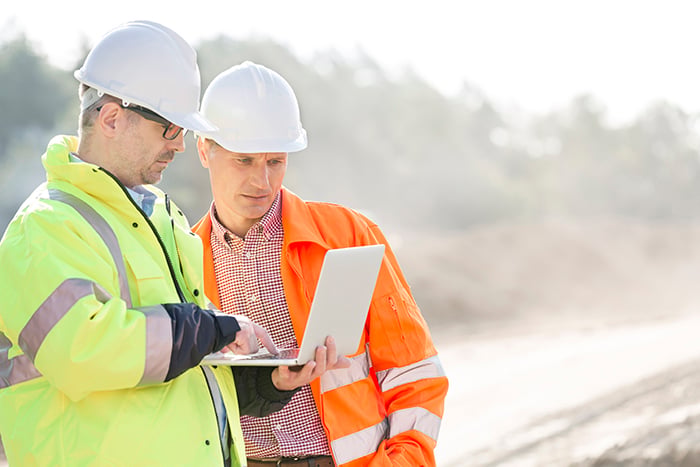 Two Construction Site Engineers Reviewing Project Data and Plans on Laptop in Field