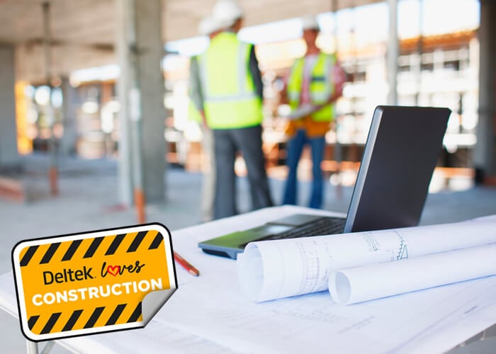 Construction workers behind blueprints and laptop on construction site