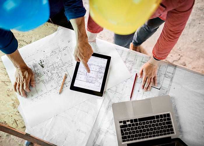 AE professionals reviewing blueprints and project plans with a tablet on a construction site