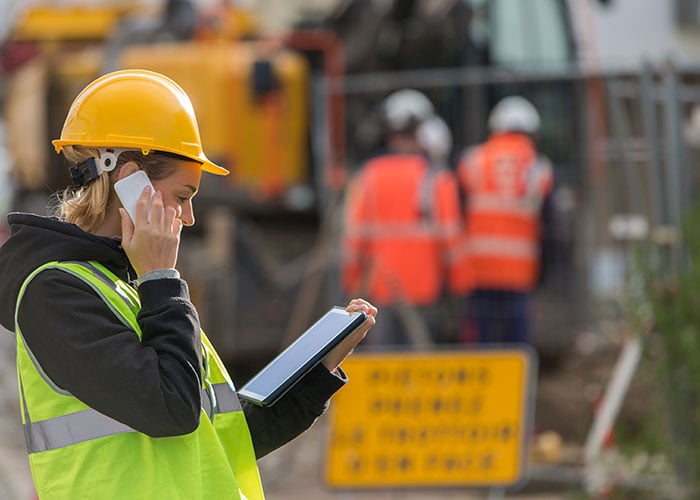 Female engineer reviewing information on a tablet while talking on the phone at a construction site