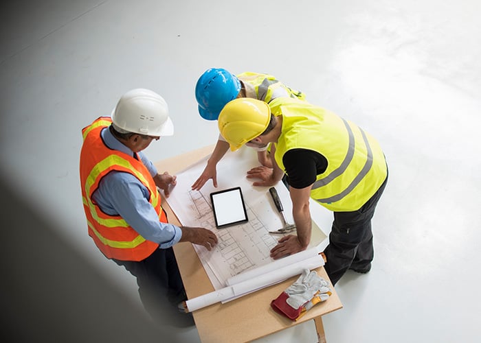 Construction Project Team Reviewing Blueprint Plans and Digital Data on Tablet at Job Site