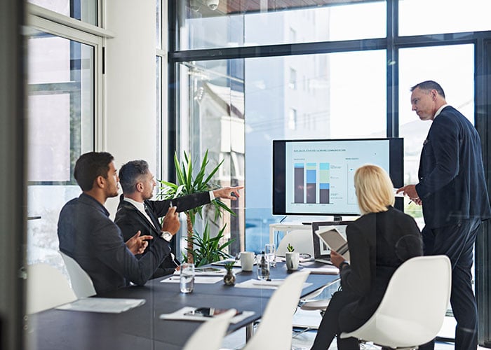 Group of people discussing a chart displayed on a monitor in a meeting room
