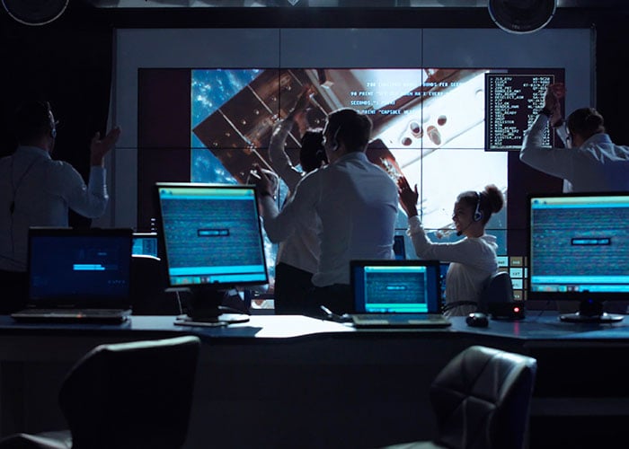 Group of supervisors celebrating docking of spaceship in dark room of mission control center