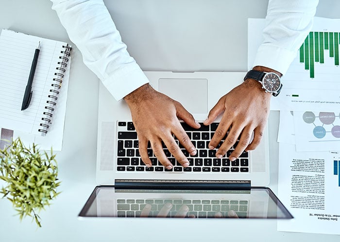 Overhead View of Business Professional Working on Laptop Surrounded by Financial Reports and Charts