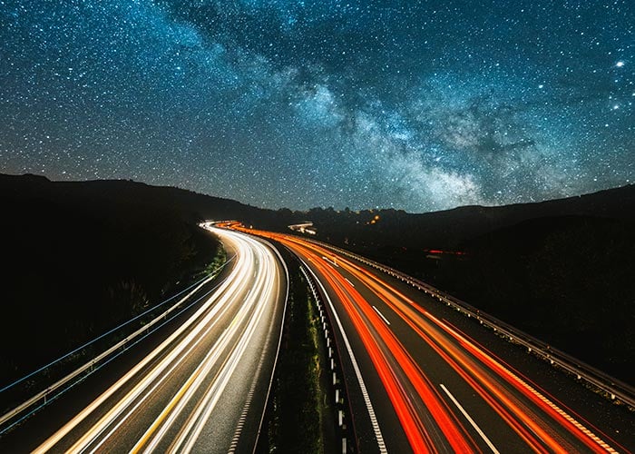 Highway Light Trails Streaming Under Milky Way Night Sky