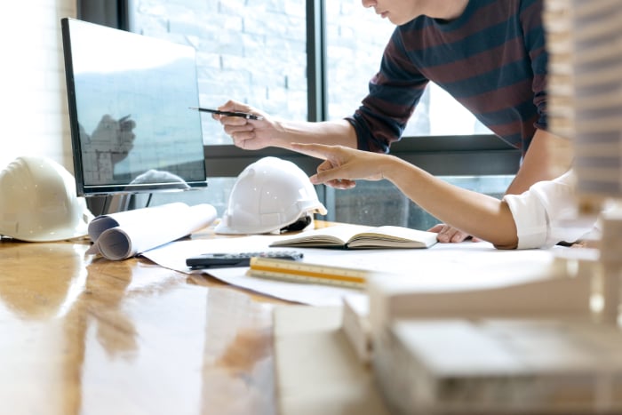Two engineers discussing architectural plans displayed on a monitor