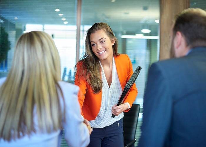 Businesswoman holding a folder and greeting coworkers