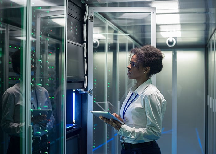 Female IT Professional Monitoring Server Infrastructure and Network Operations on Tablet in Data Center