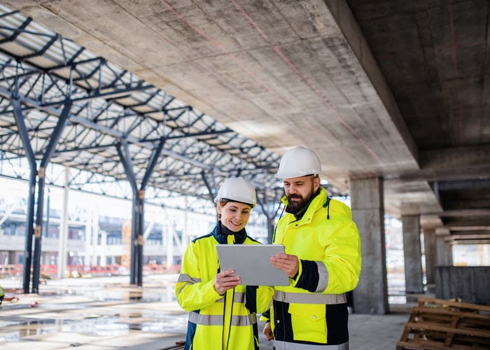 Two workers on a construction site looking at a tablet device