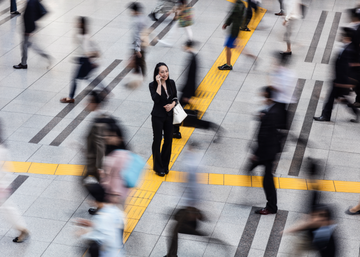 Female business woman standing still talking on mobile phone in the middle of a busy area of people walking
